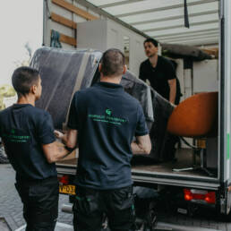 Drie verhuizers die meubels een een vrachtwagen laden voor meubeltransport.